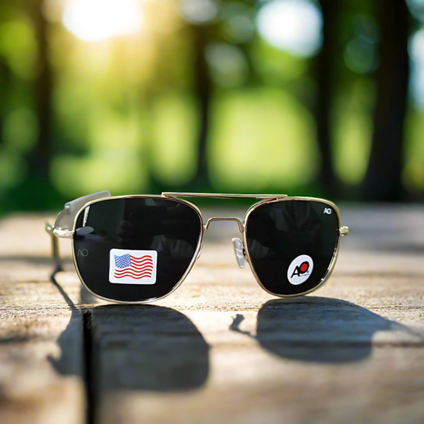 A pair of sunglasses with a gold frame and black lenses, featuring a small American flag on the side.