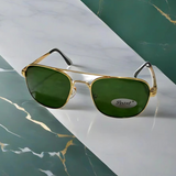 Gold-framed sunglasses with green lenses on a marble surface
