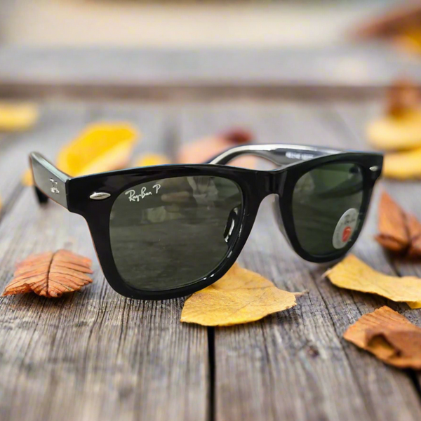 Black Ray-Ban sunglasses on a wooden surface with autumn leaves