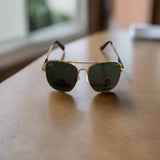 Gold-framed sunglasses with green lenses on a wooden surface