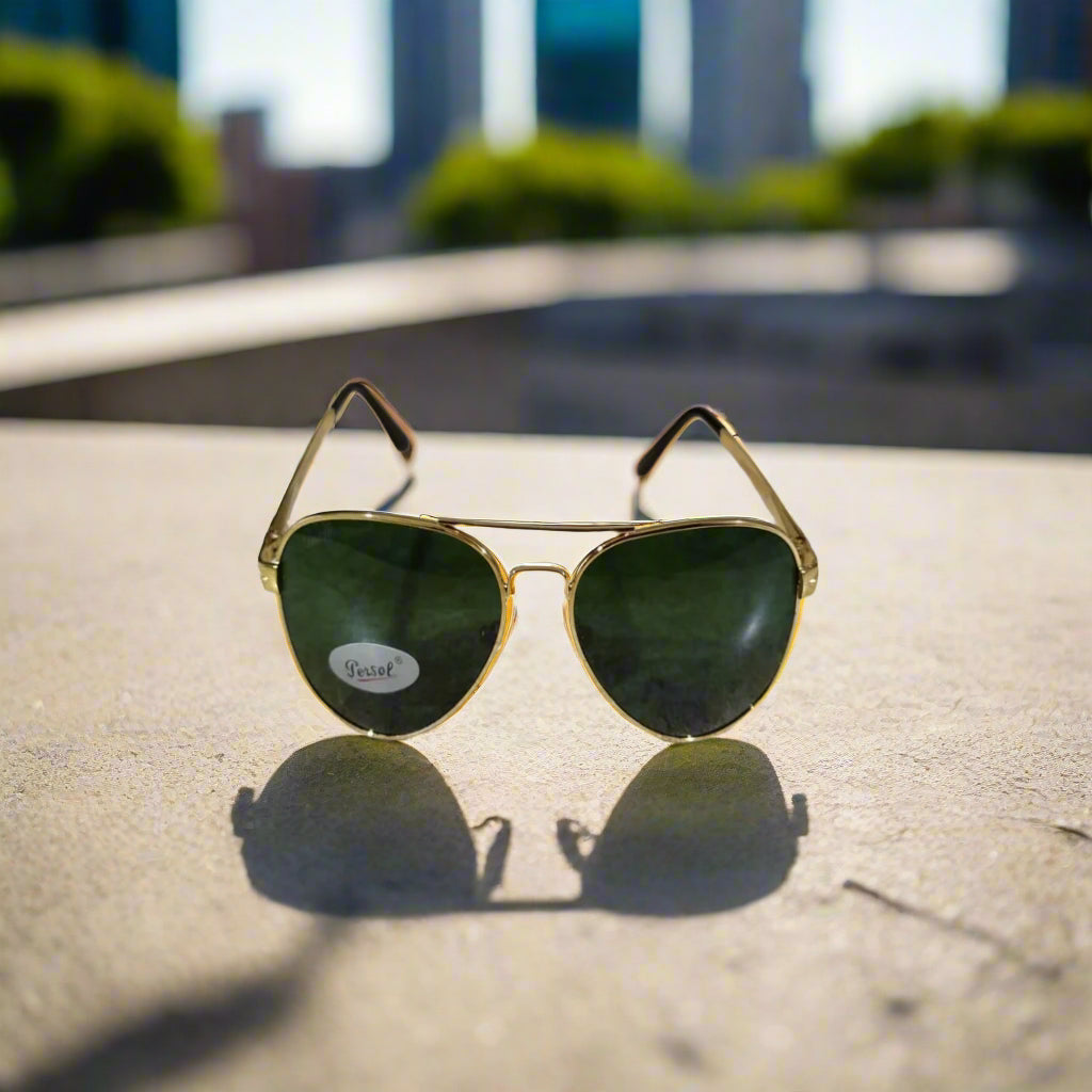 Gold-framed sunglasses with green lenses on a textured surface