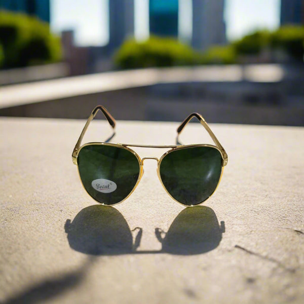 Gold-framed sunglasses with green lenses on a textured surface