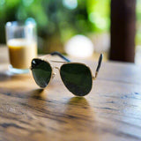 Aviator sunglasses with gold frame and dark lenses on a textured surface.