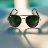 Aviator sunglasses with gold frame and green lenses on a textured surface