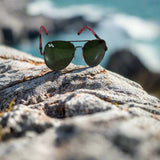 Sunglasses with red frames and green lenses on a textured surface