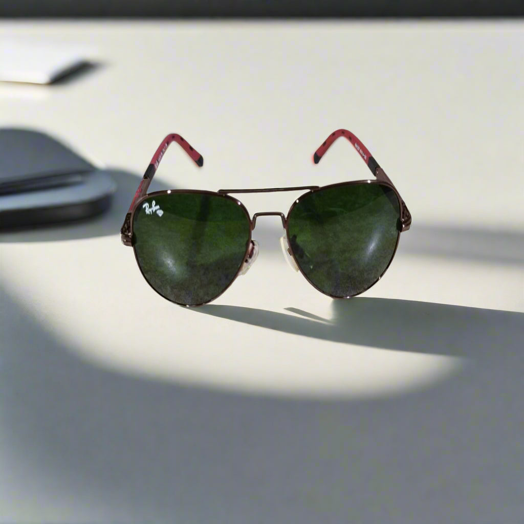 Aviator sunglasses with red frames and green lenses on a textured surface