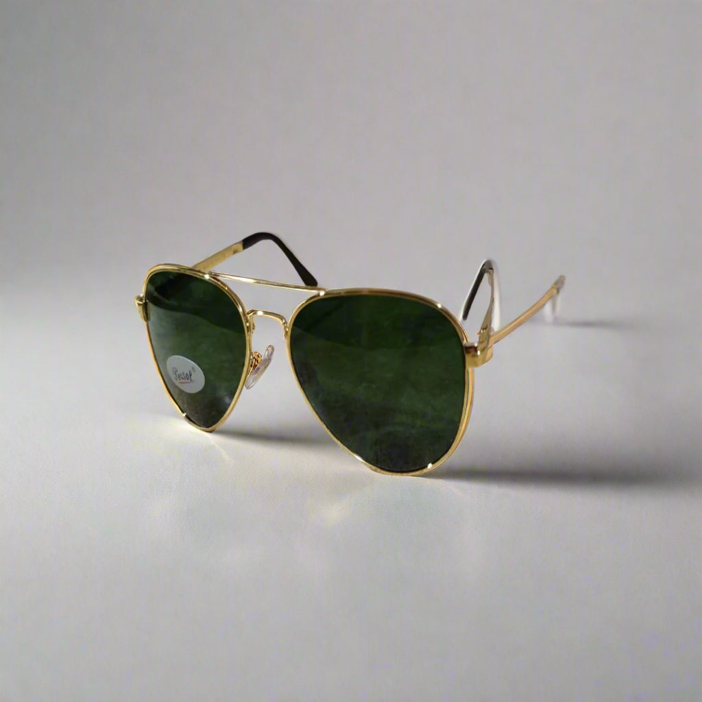 Aviator sunglasses with gold frame and green lenses on a textured surface.