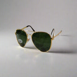 Aviator sunglasses with gold frame and green lenses on a textured surface.