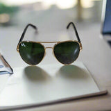 Gold-framed sunglasses with green lenses on a textured surface