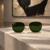 Ray-Ban aviator sunglasses with green lenses and gold frames, displayed on a light stone pedestal in a gallery setting.