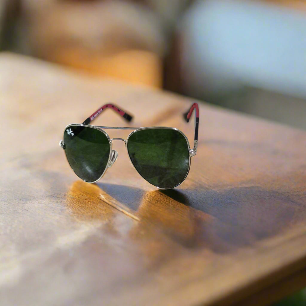 Aviator sunglasses with green lenses and red earpieces on a textured surface.
