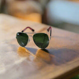 Aviator sunglasses with green lenses and red earpieces on a textured surface.